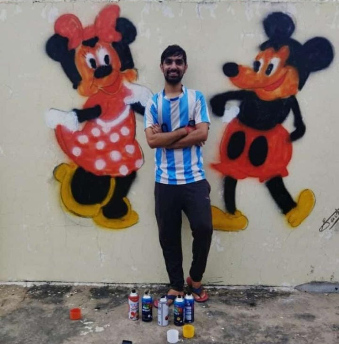 Sachin Upadhyay next to a hand-painted Mickey and Minnie Mouse mural